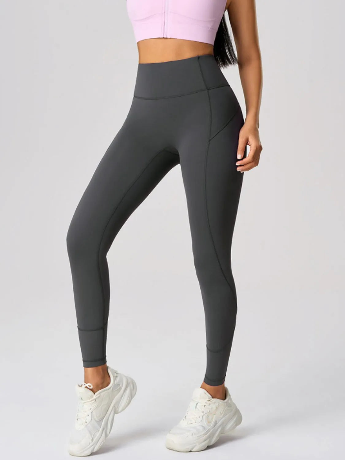 Person wearing dark gray leggings and white sneakers on a light gray background