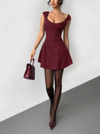 Woman wearing a burgundy dress holding a matching handbag on a gray background