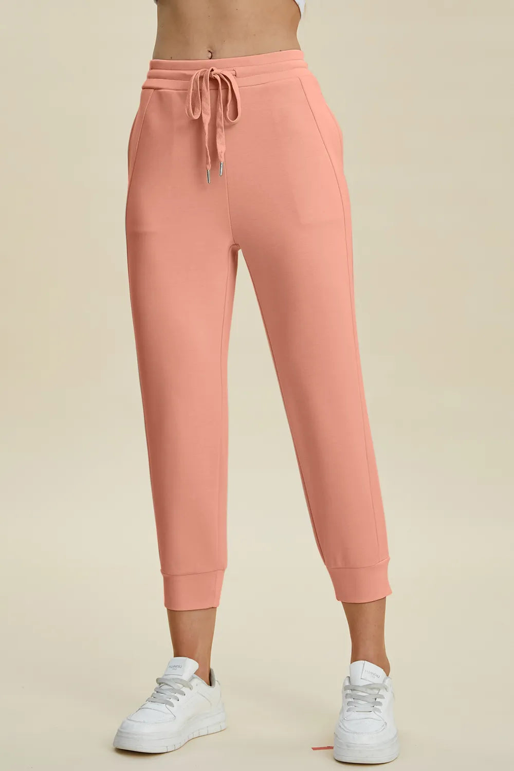 Peach-colored sweatpants worn by a person on a beige background
