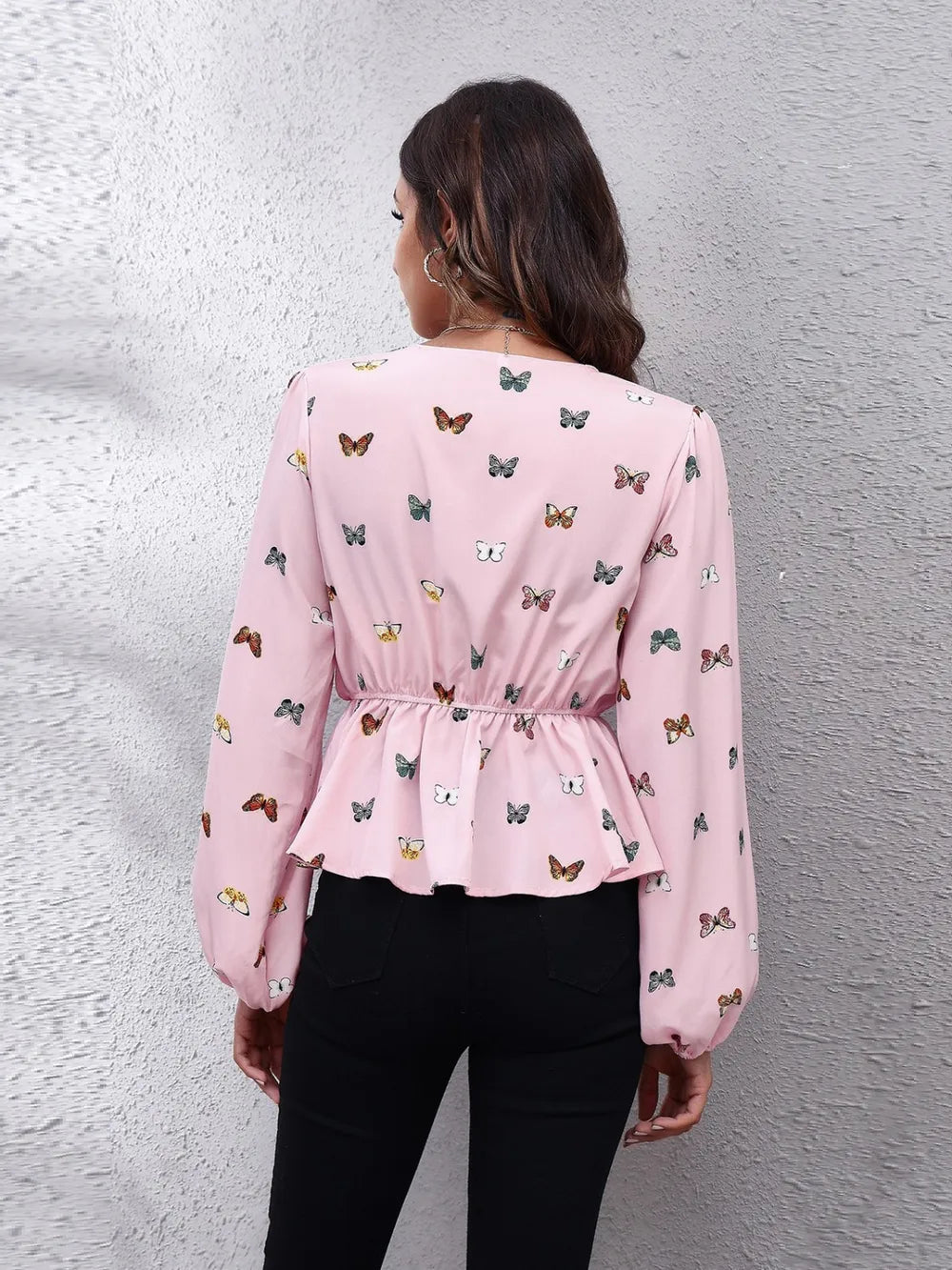 Woman wearing a pink blouse with butterfly pattern against a gray wall