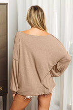 Person wearing a beige oversized sweater in a room with white curtains.