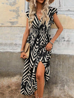 Woman wearing a black and white striped dress with a patterned hat against a rustic wall.