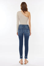 Woman wearing blue jeans and a beige one-shoulder top on a white background