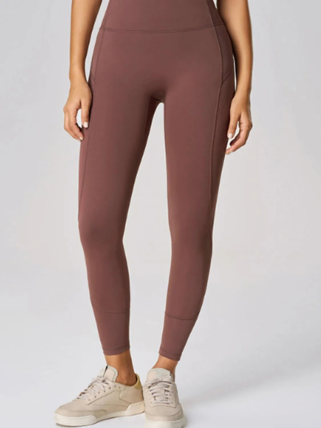 Person wearing brown leggings with beige sneakers on a light gray background