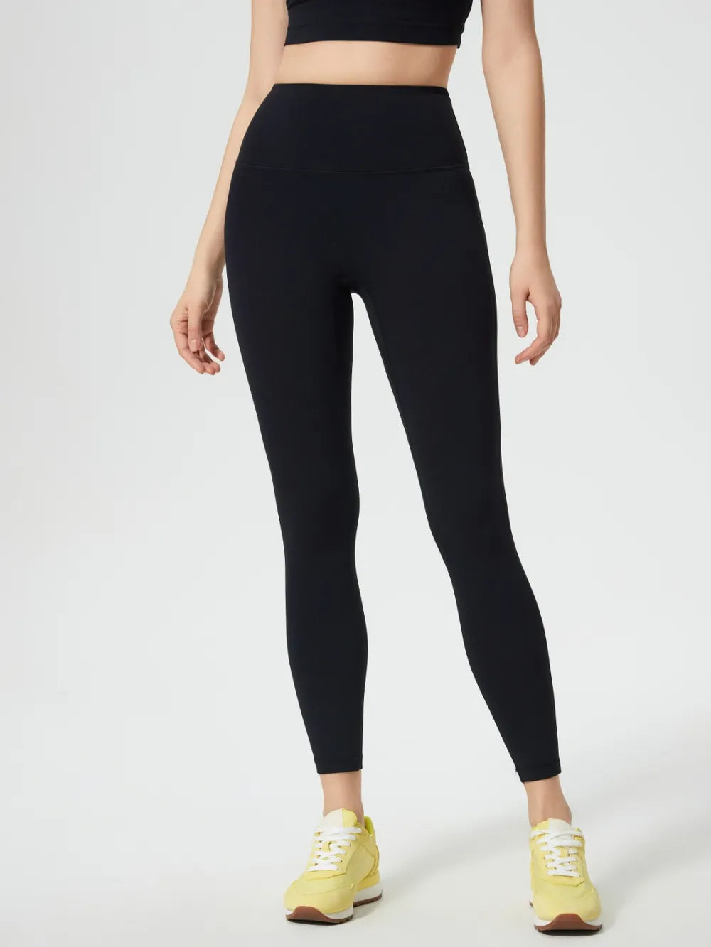Person wearing black leggings and a black crop top on a white background