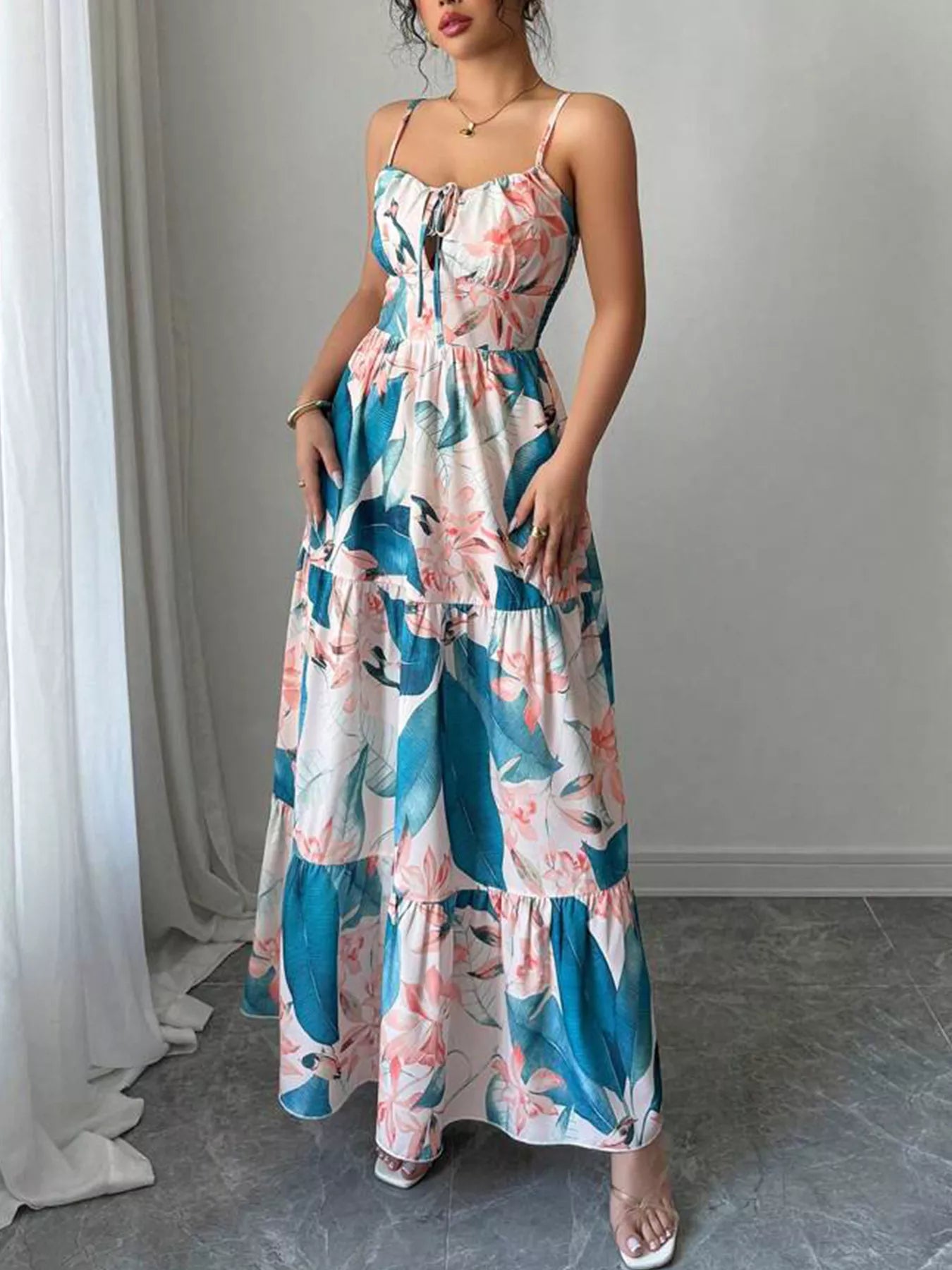 Woman wearing a floral dress standing in a room with gray flooring and white curtains.