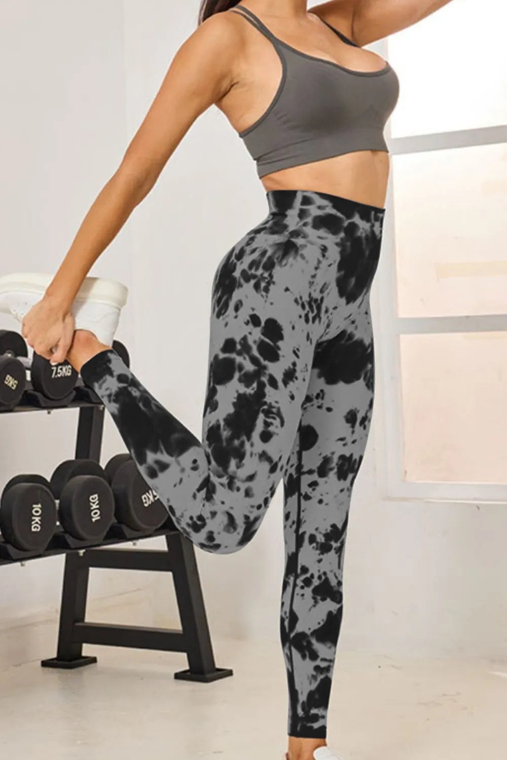 Person wearing a gray sports bra and tie-dye leggings in a gym setting.