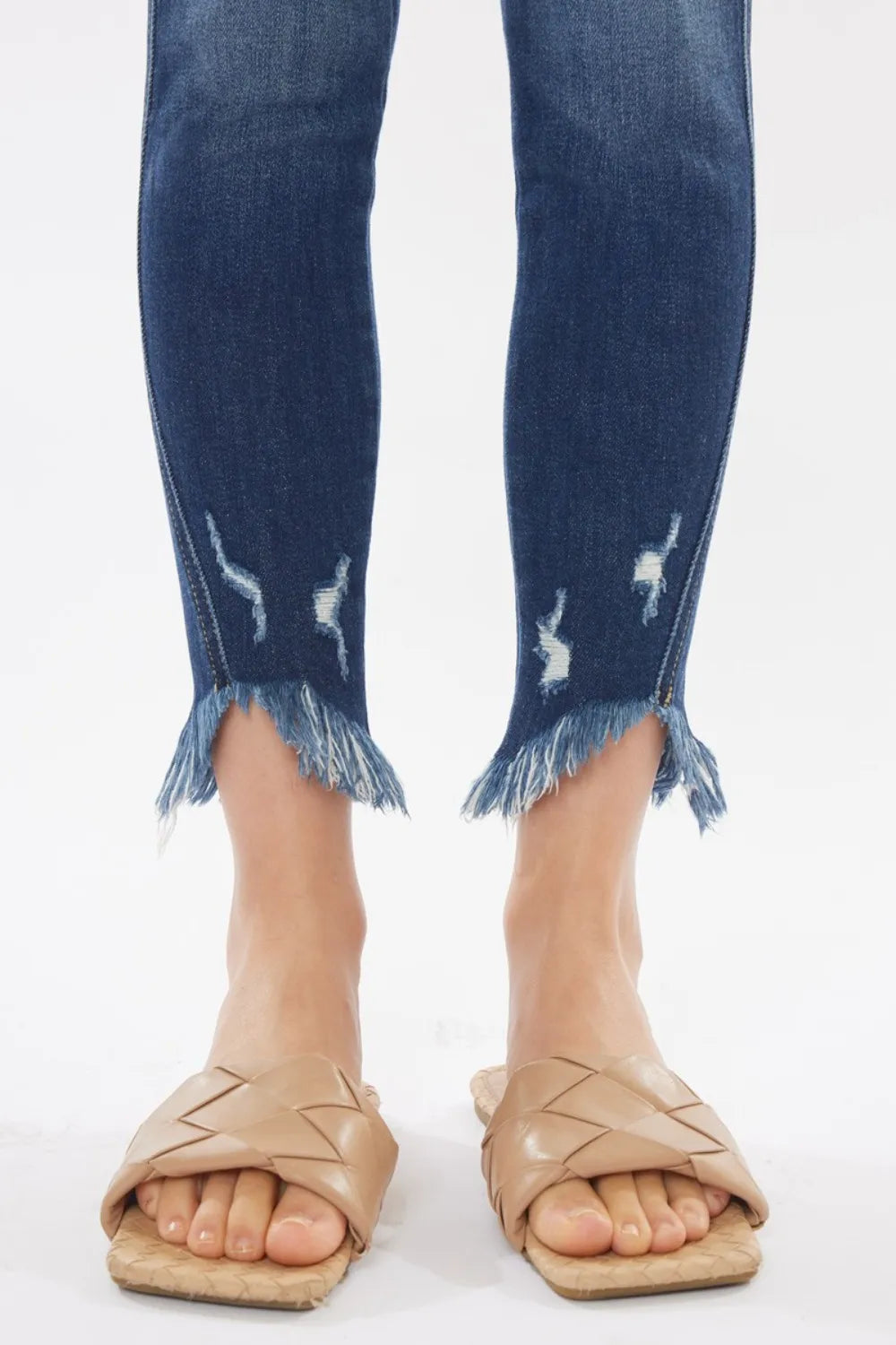 Blue jeans with frayed cuffs worn by a person on a white background