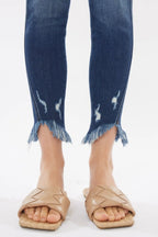 Blue jeans with frayed cuffs worn by a person on a white background