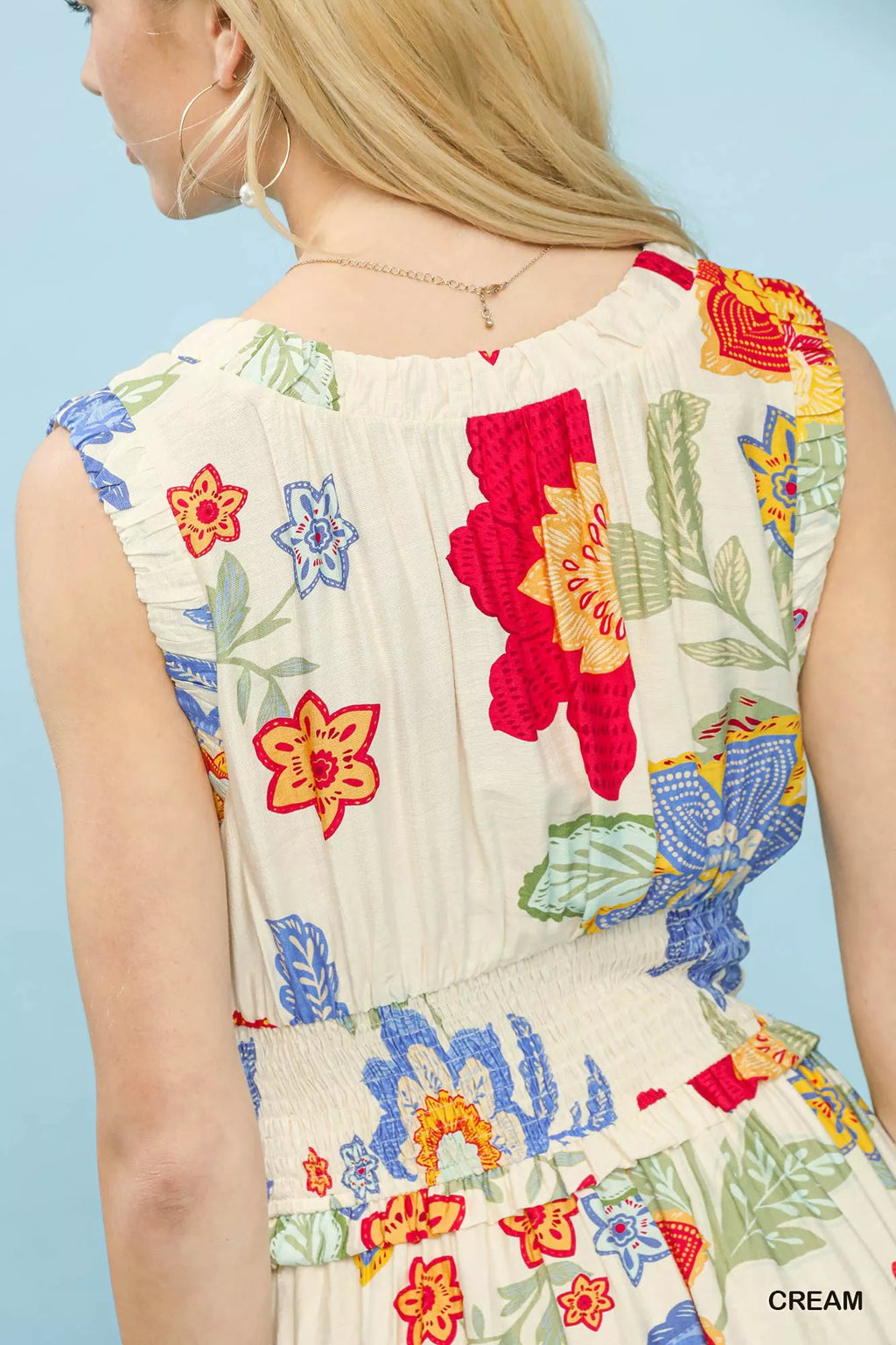 Woman wearing a sleeveless dress with colorful floral embroidery on a light blue background