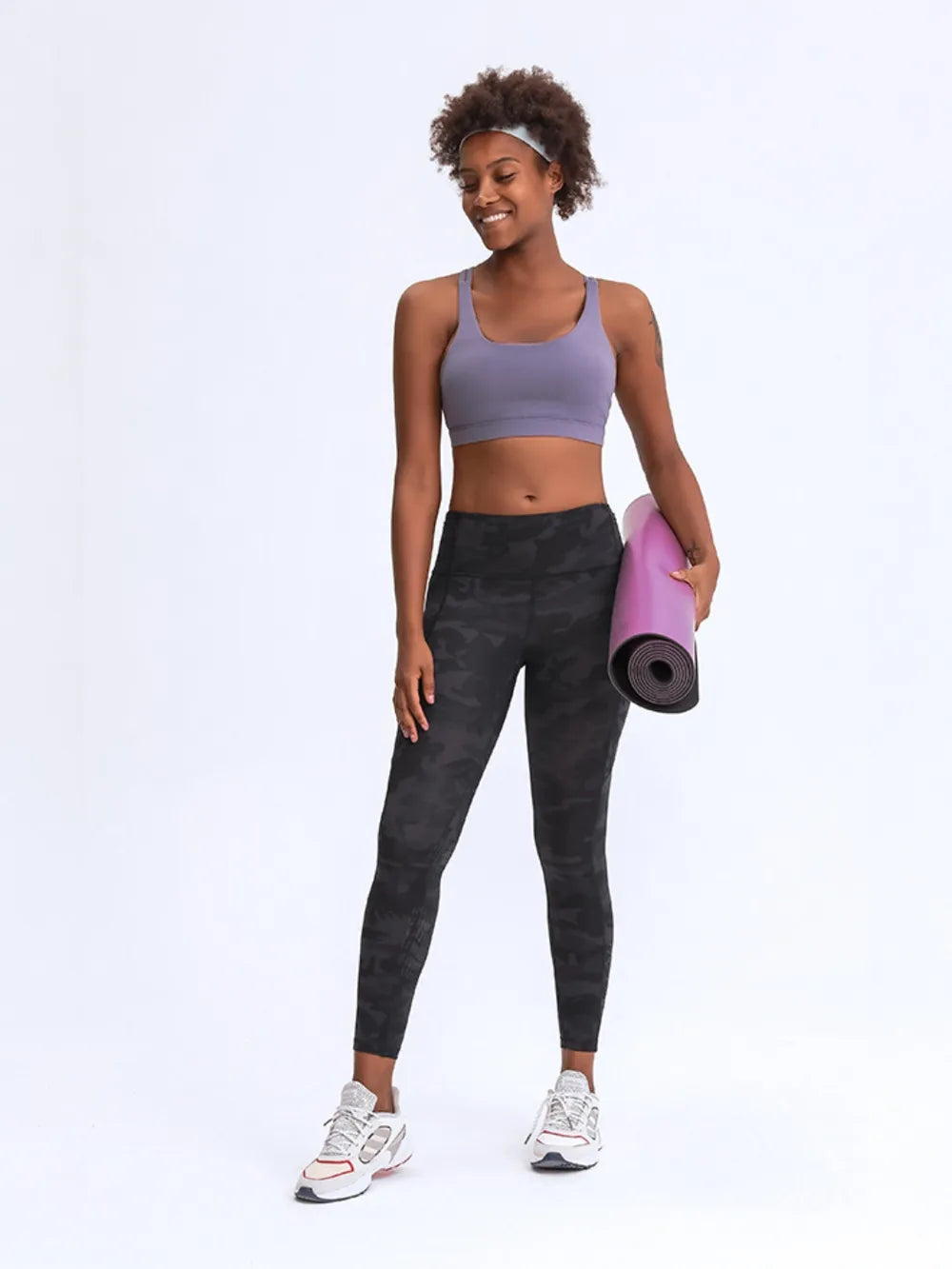 Woman in athletic wear holding a pink yoga mat on a white background