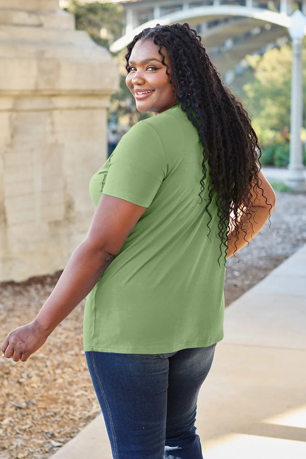 Woman wearing a green t-shirt and blue jeans standing outdoors.