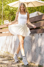 Woman in a white outfit standing outdoors with a wooden bench and umbrella in the background