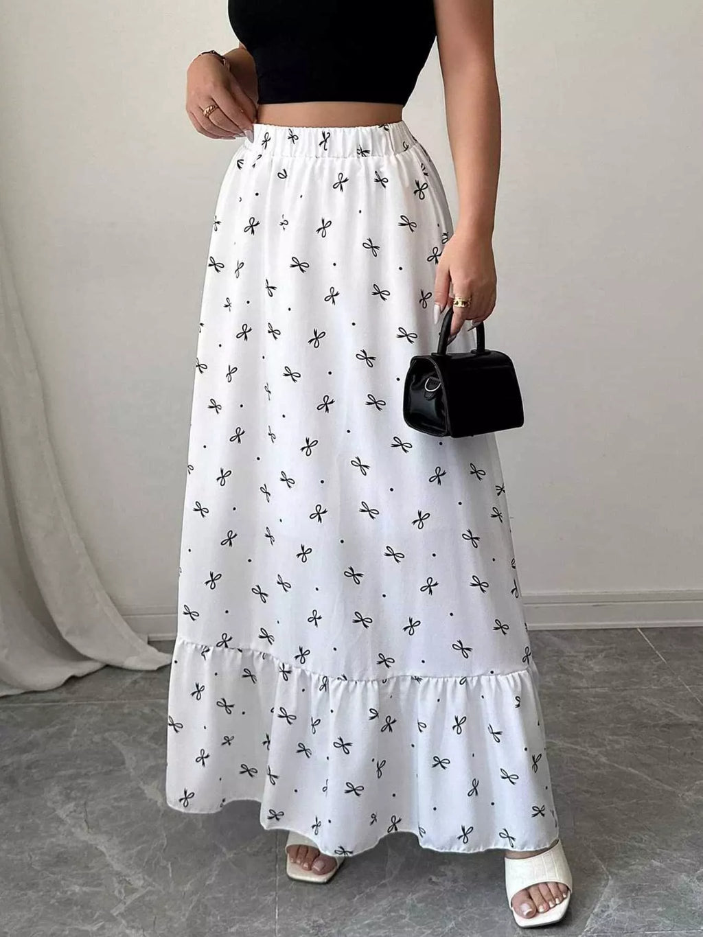 Person wearing a white skirt with black patterns and holding a black handbag.