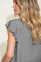 Woman wearing a gray top with ruffled sleeves against a plain background