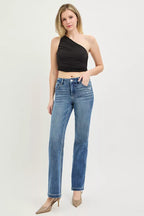 Woman wearing a black one-shoulder top and blue jeans on a white background
