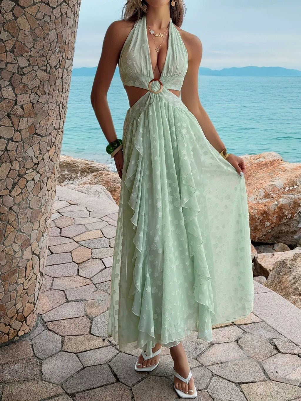 Woman in a light green dress standing by a stone wall with ocean view