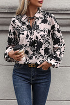 Woman wearing a black and white floral blouse with blue jeans, holding a coffee cup.