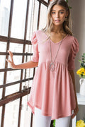 Woman wearing a pink dress standing indoors with a window and decor in the background