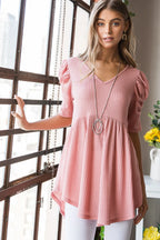 Woman wearing a pink dress standing indoors with a window and decor in the background