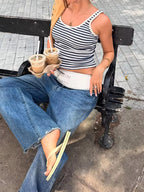 Woman sitting on a bench holding iced drinks, wearing a striped top and jeans.
