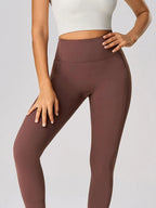 Person wearing brown leggings and a white top on a light gray background
