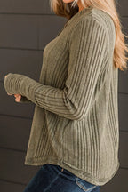 Person wearing a green ribbed sweater against a dark background