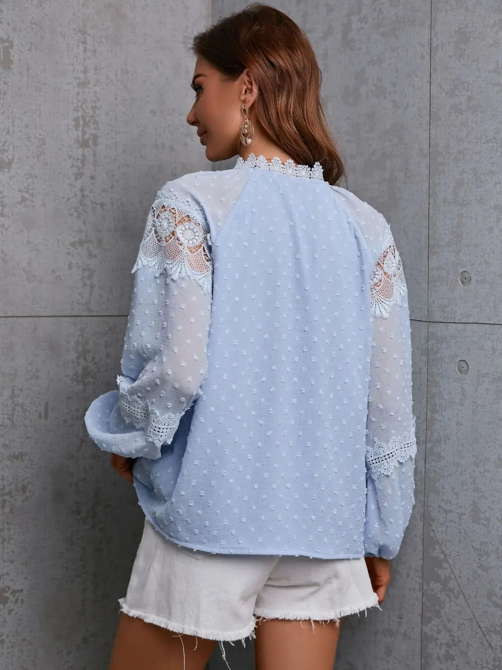 Woman wearing a light blue lace top against a gray wall
