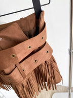 Brown suede bag with fringe details on a hanger against a white background