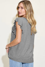 Woman wearing a gray sleeveless top with ruffle details on a plain background