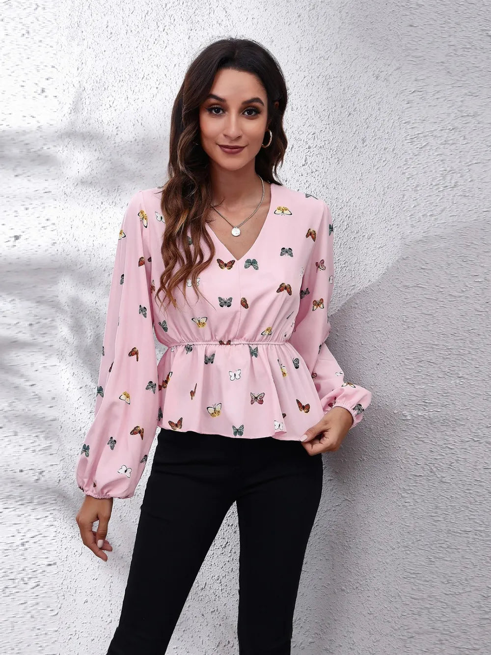 Woman wearing a pink blouse with butterfly pattern against a textured white wall