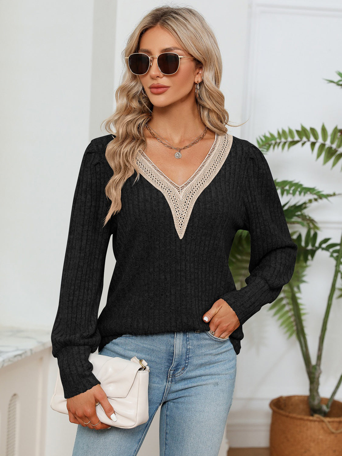 Woman wearing a black sweater with lace details, blue jeans, and sunglasses indoors.