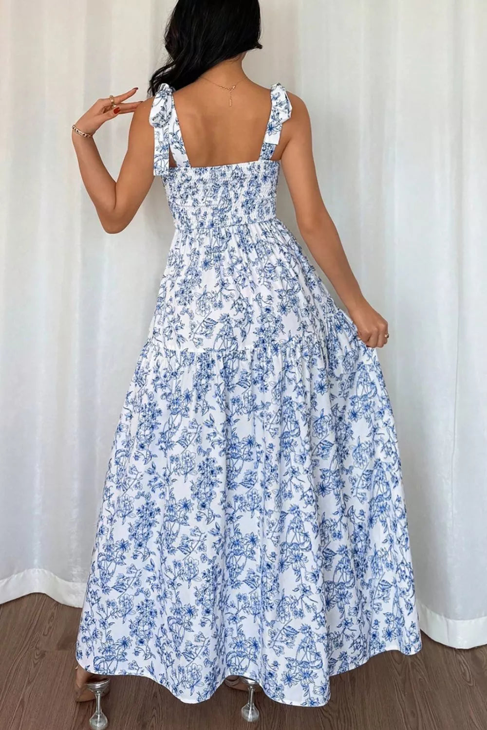 Woman wearing a blue floral dress against a white curtain background