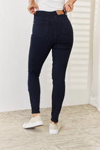 Person wearing navy blue jeans and white sneakers in a minimal indoor setting