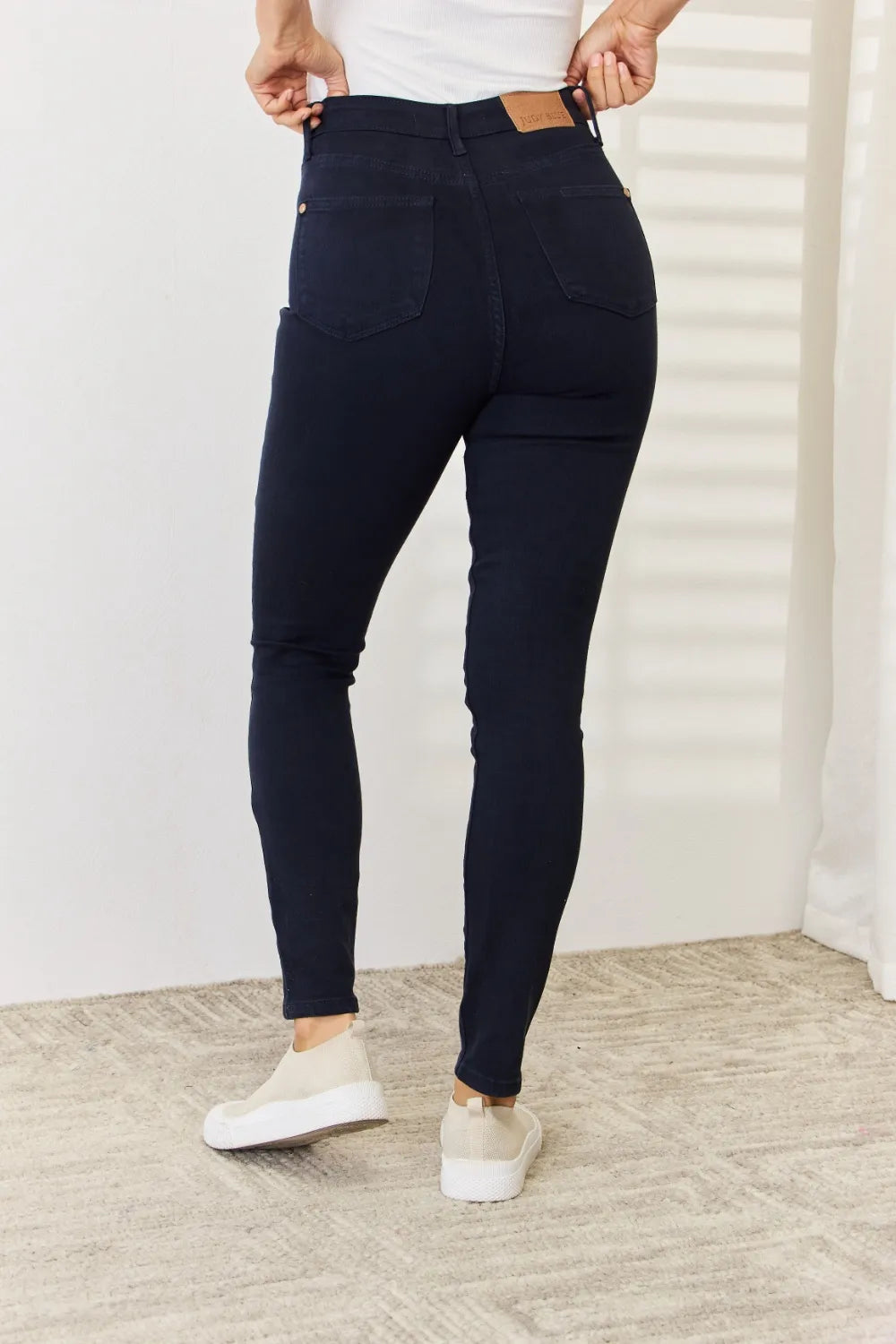 Person wearing navy blue jeans and white sneakers in a minimal indoor setting