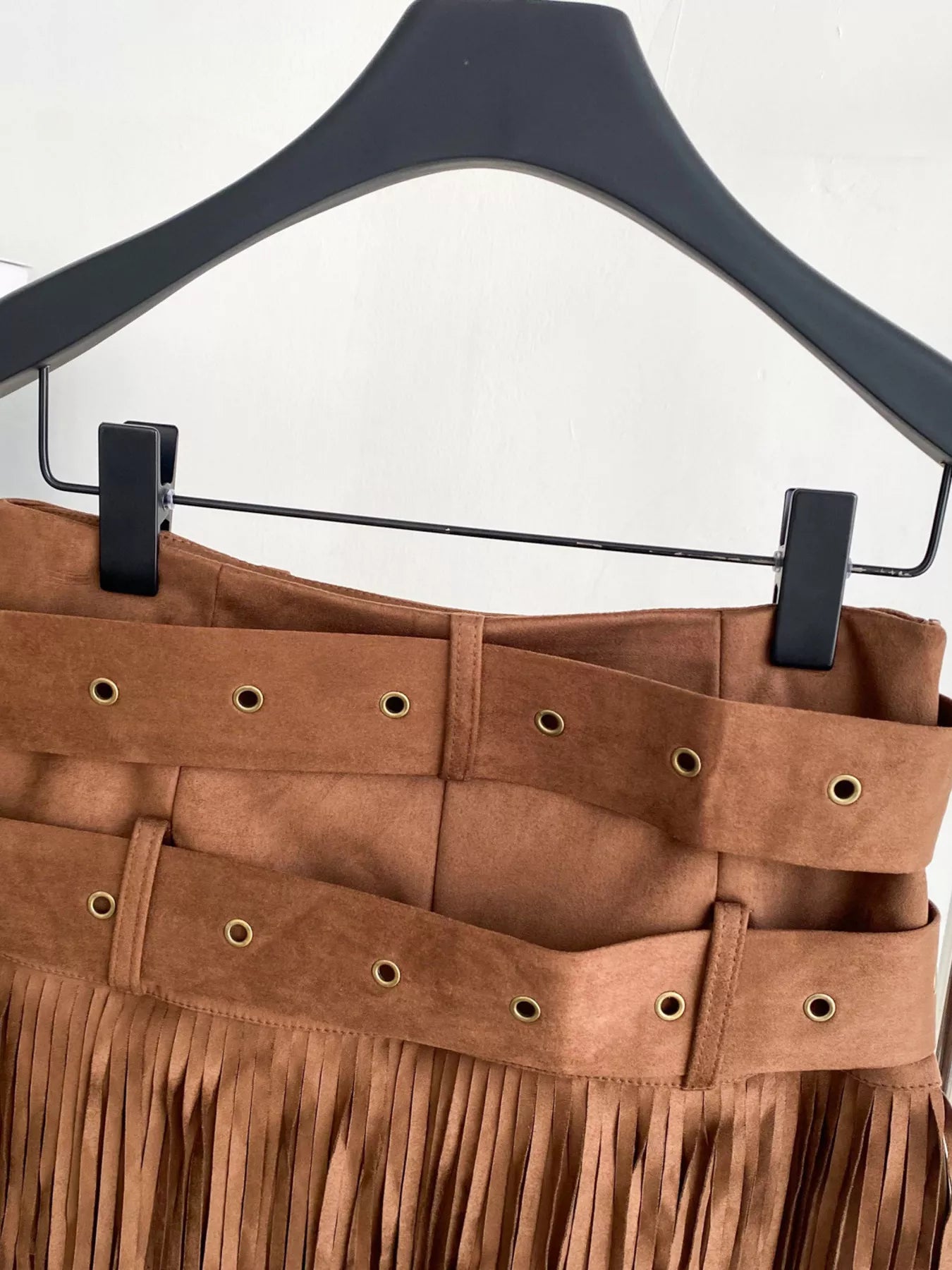Brown fringed skirt on a hanger against a white background