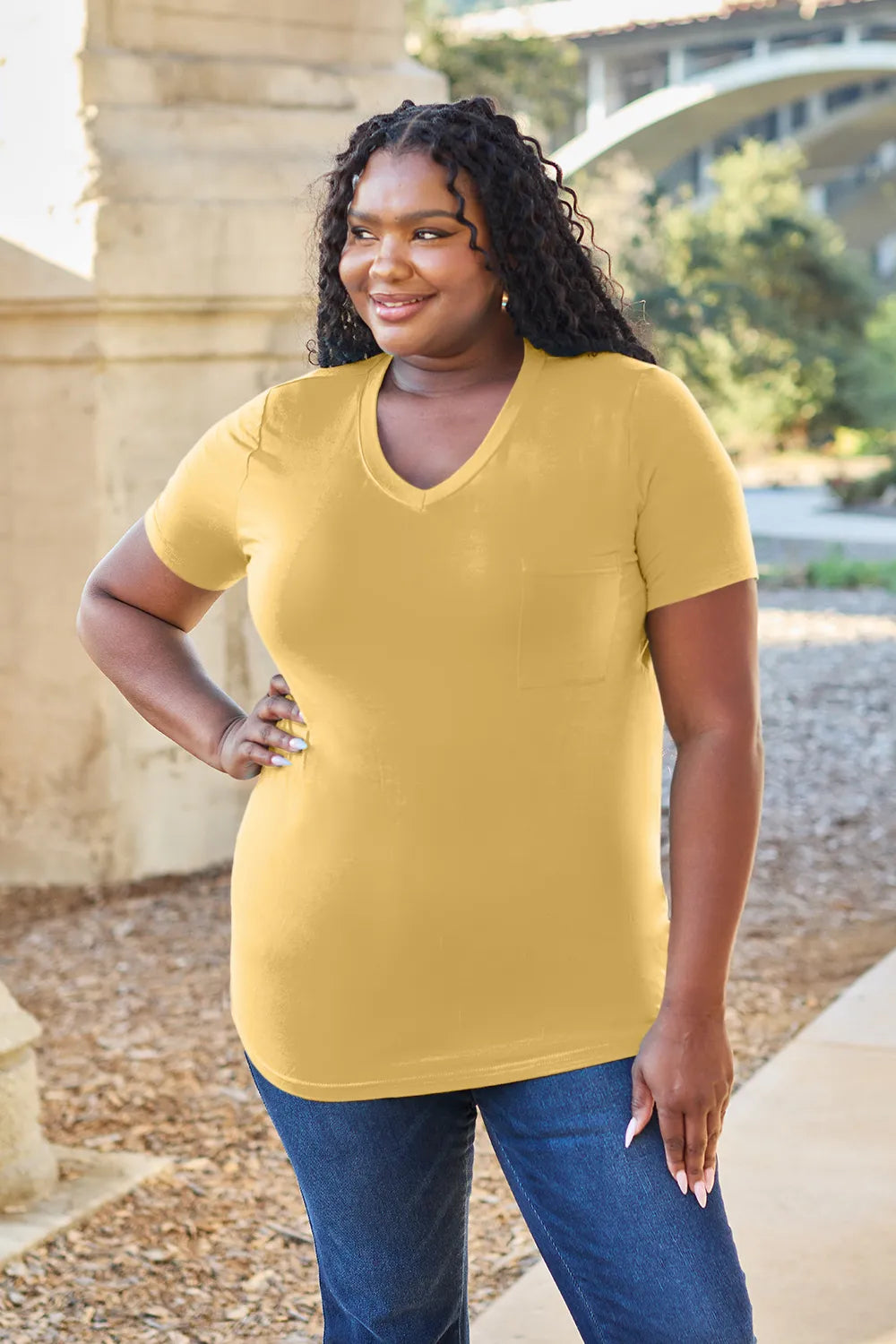 Woman wearing a yellow t-shirt and blue jeans standing outdoors with a blurred background