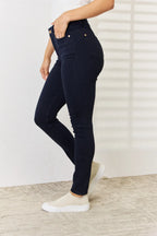 Person wearing navy blue jeans and white sneakers on a light wooden floor.