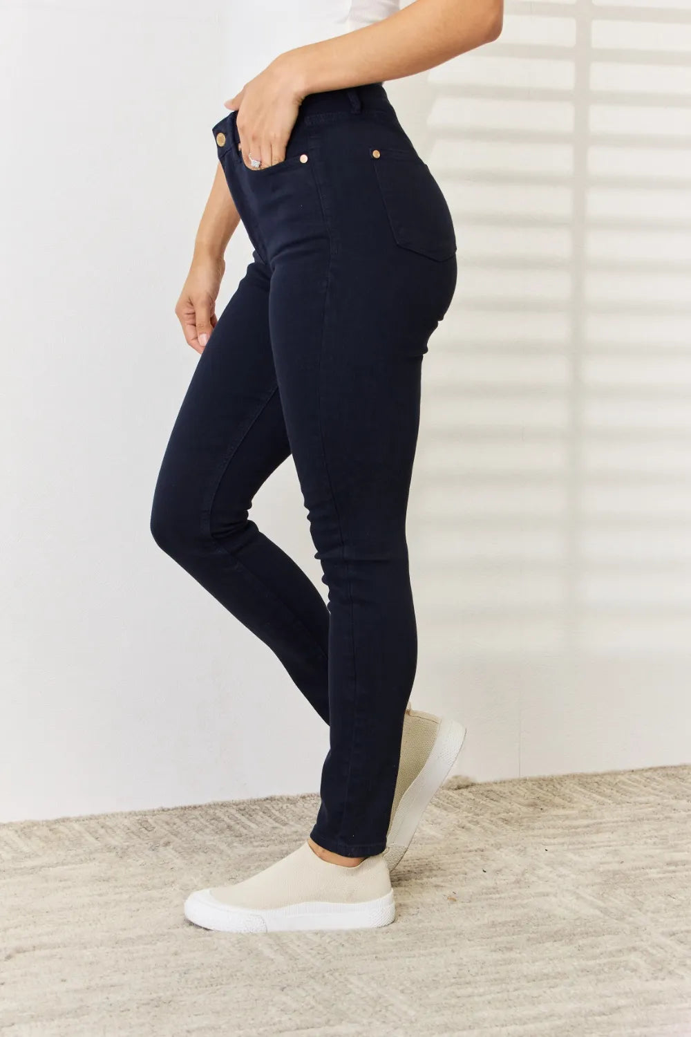 Person wearing navy blue jeans and white sneakers on a light wooden floor.