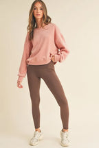 Woman wearing a pink sweatshirt and brown leggings on a beige background