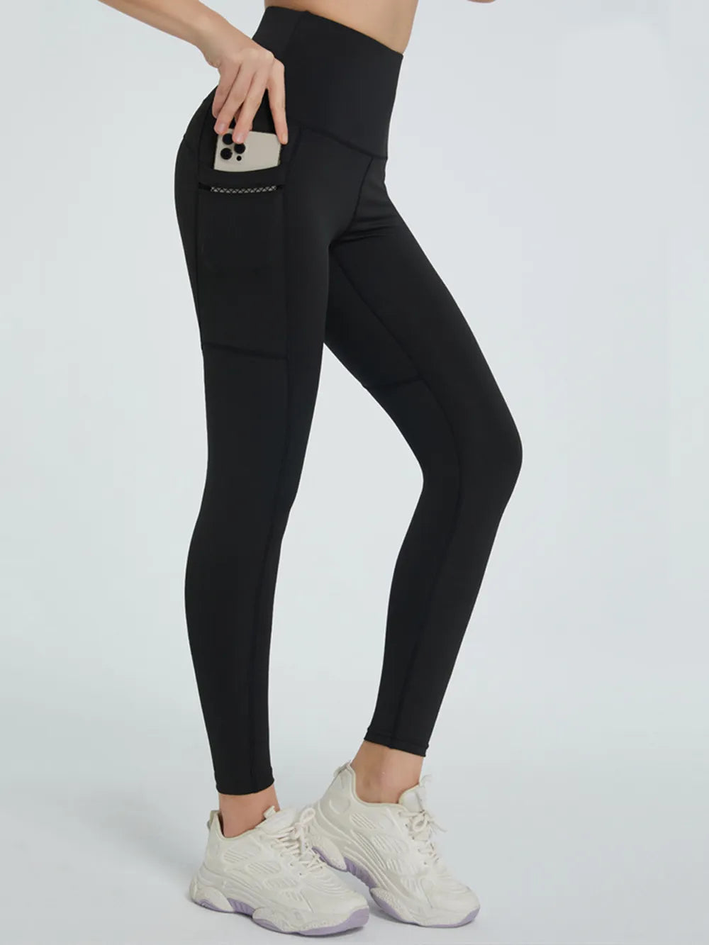Person wearing black leggings with a pocket holding a phone on a white background