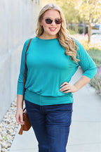 Woman wearing a teal top and blue jeans outdoors.