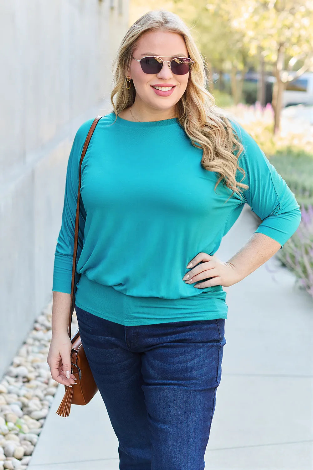 Woman wearing a teal top and blue jeans outdoors.