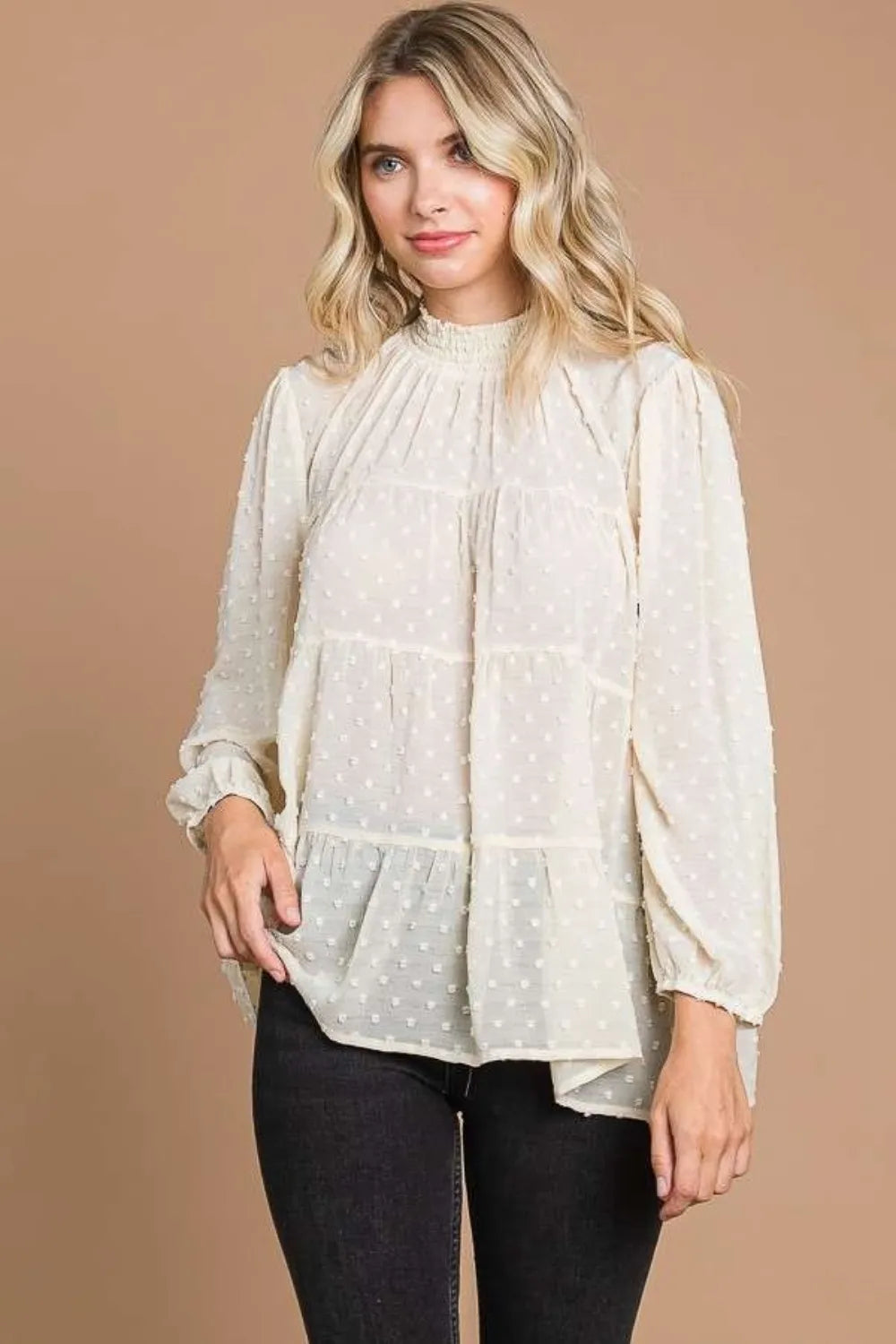 Woman wearing a white blouse with long sleeves against a beige background