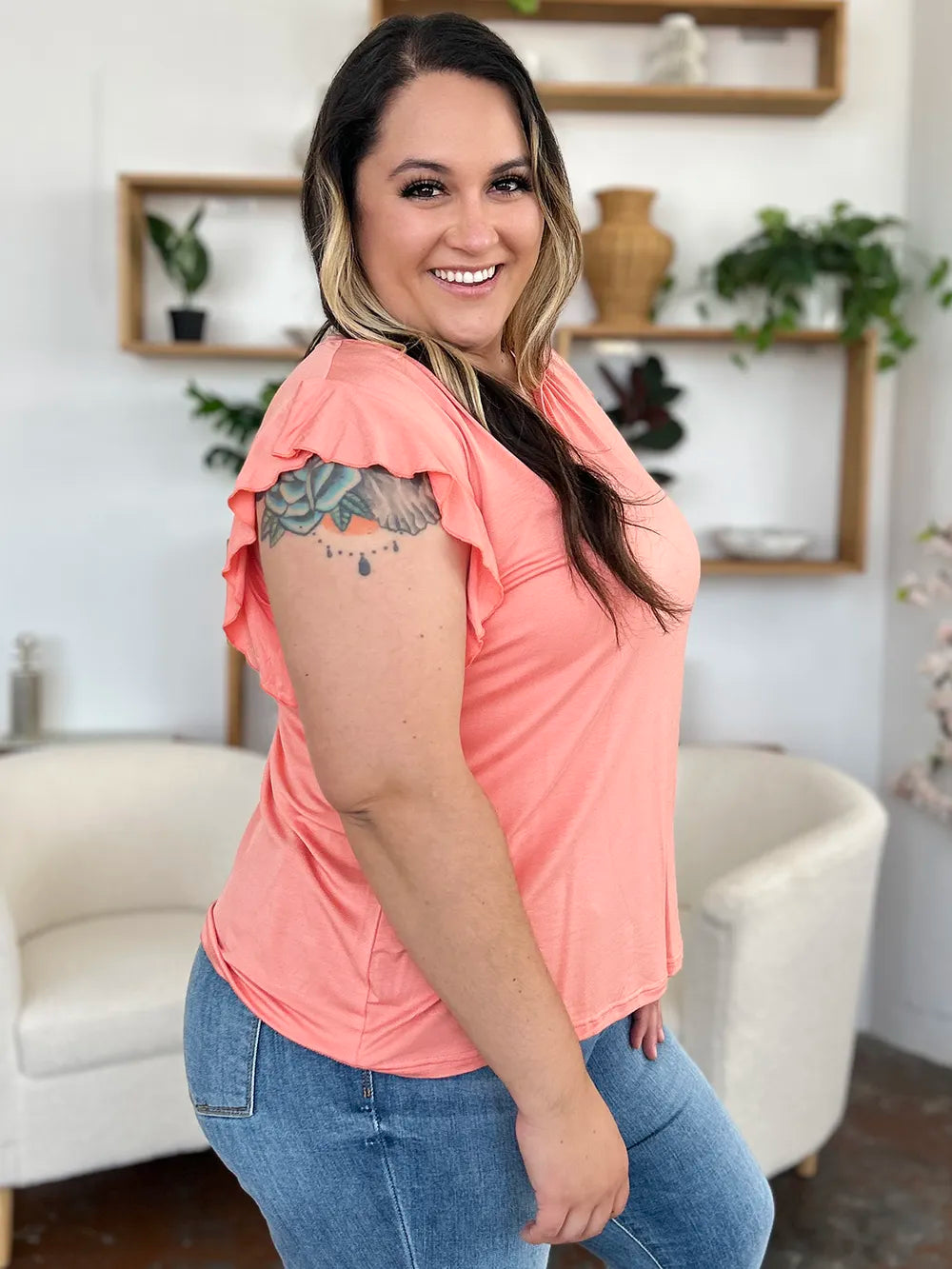 Woman wearing a peach-colored top and blue jeans in a living room setting.