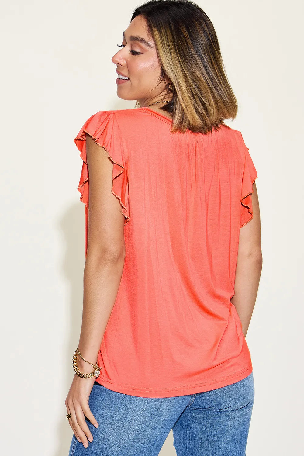 Woman wearing a coral top with ruffled sleeves against a white background