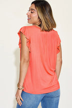 Woman wearing a coral top with ruffled sleeves against a white background