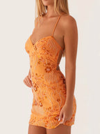 Woman wearing an orange dress with floral patterns on a plain background