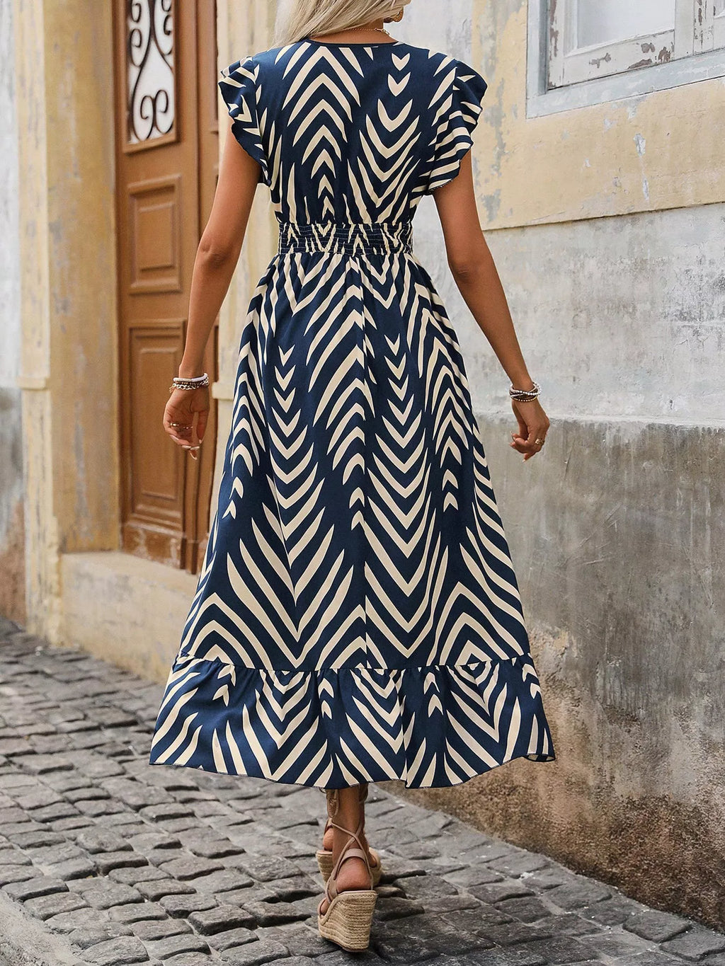 Woman wearing a blue and white patterned dress on a cobblestone street.