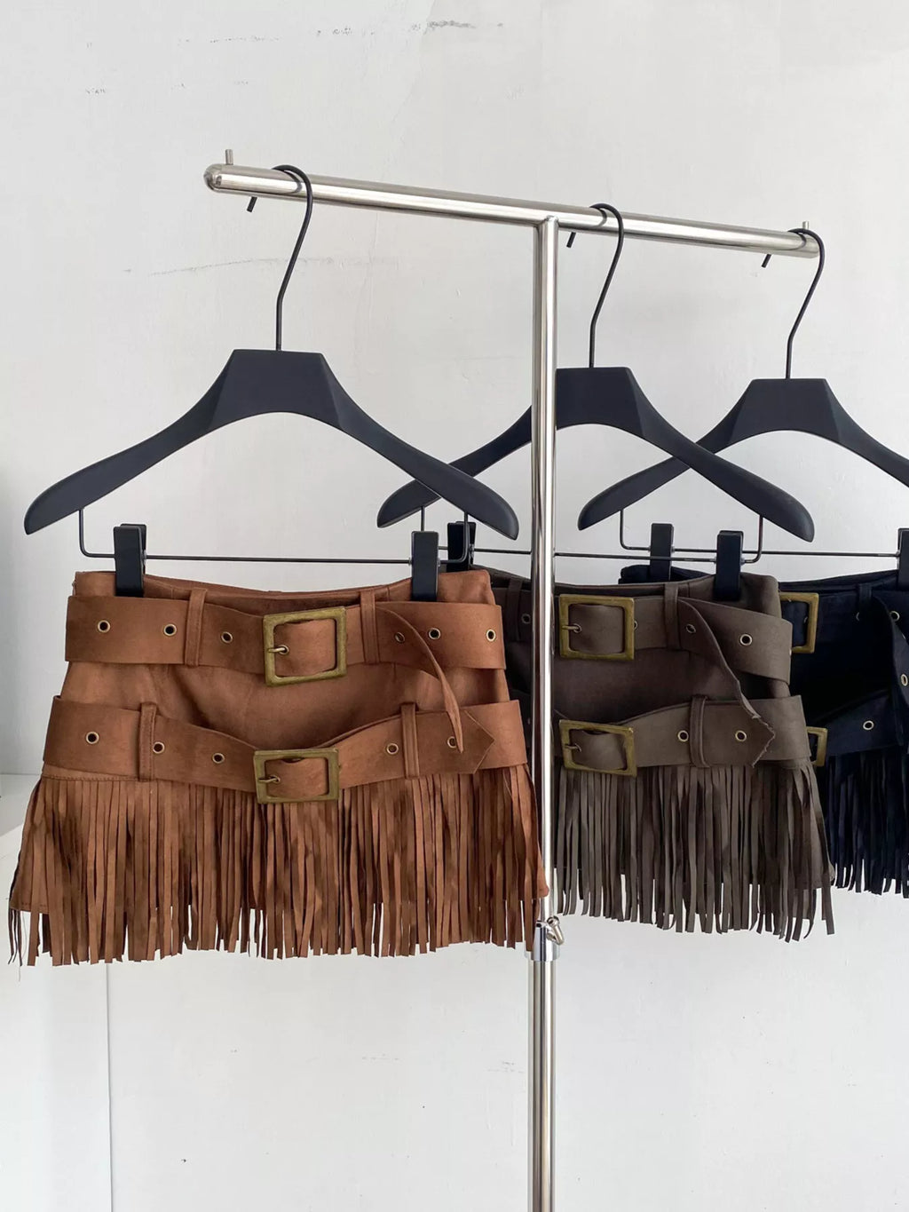 Three fringed belts on hangers against a white background